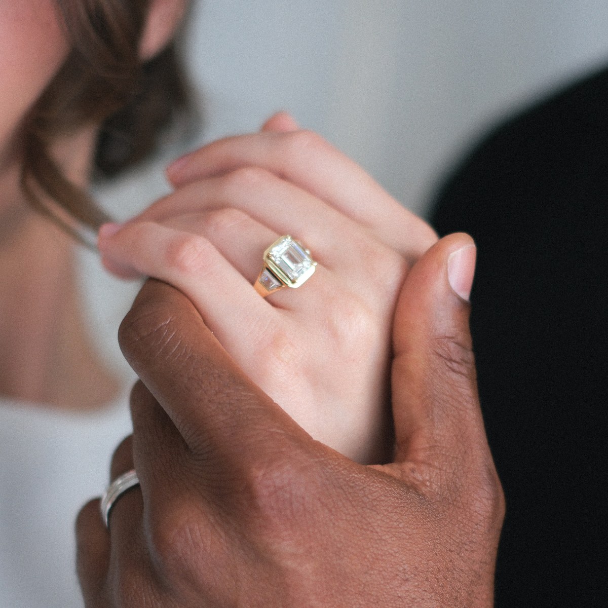 Emerald cut engagement ring held between two hands