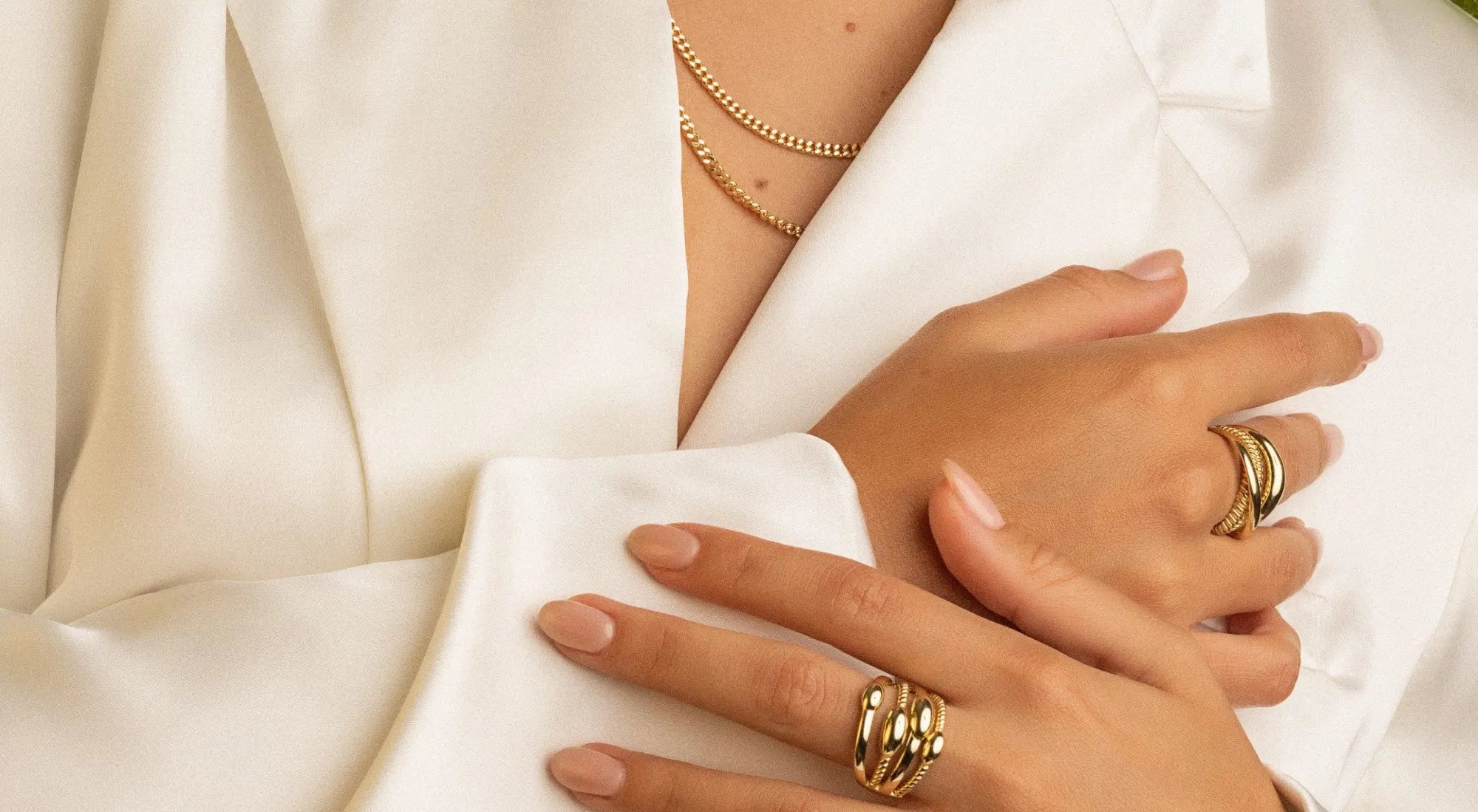 Stacked gold rings and a fine chain necklace worn with an ivory silk blouse